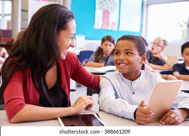 Teacher helping elementary school boy using tablet computer
