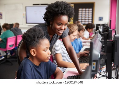 Teacher Helping Female Pupil Line Of High School Students Working At Screens In Computer Class