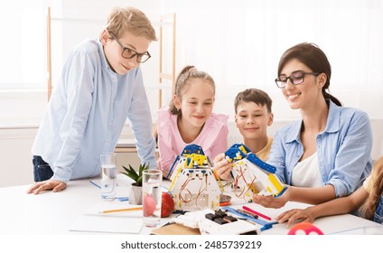 A teacher is helping her students build robots during a classroom activity. They are smiling and working together on the project. Positive and engaging learning environment for STEM education.