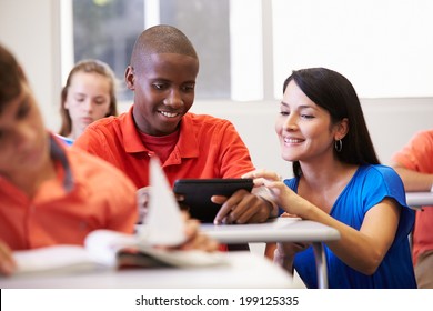 Teacher Helping Male High School Student In Classroom