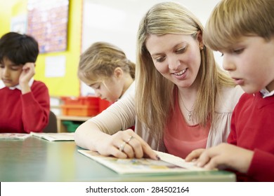 Teacher Helping Male Pupil With Reading At Desk - Powered by Shutterstock