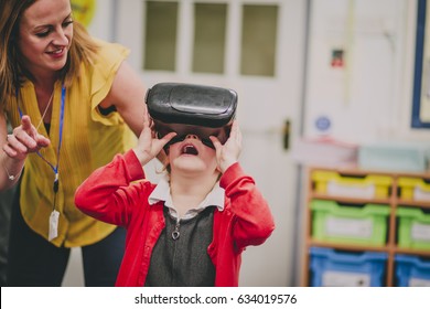 Teacher Is Helping One Of Her Primary School Students Use A Virtual Realtiy Headset In The Classroom.