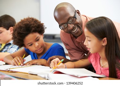 Teacher Helping Pupils Studying At Desks In Classroom - Shutterstock ID 139406252