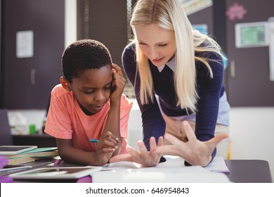 Teacher helping schoolgirl with her homework in classroom at school