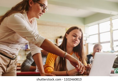Teacher helping student in classroom. Lecturer pointing at laptop screen and showing something to female student.