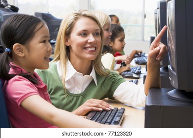 Teacher Helping Student At Computer Terminal With Students In Background (depth Of Field/high Key)