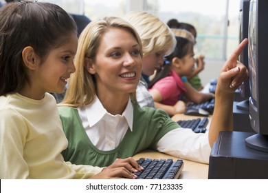 Teacher Helping Student At Computer Terminal With Students In Background (depth Of Field/high Key)