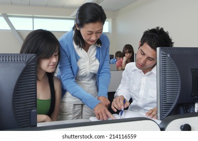 Teacher Helping Two Students Working In Computer Classroom