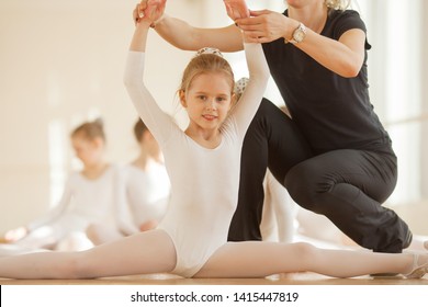 Teacher Helping Young Cute Balerina To Sit On Split In Ballet Class 