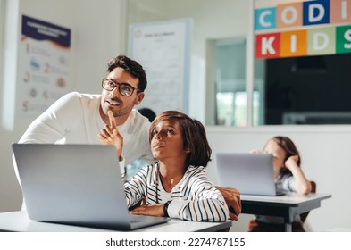 Teacher helping a young student understand a coding exercise in a class. At his desk, the educator provides the young kid with individual attention, guiding him through computer programming. - Powered by Shutterstock