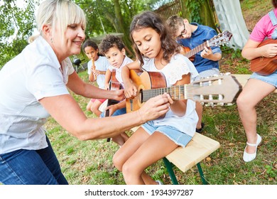 Teacher helps children learn to play guitar in class at summer camp or summer camp