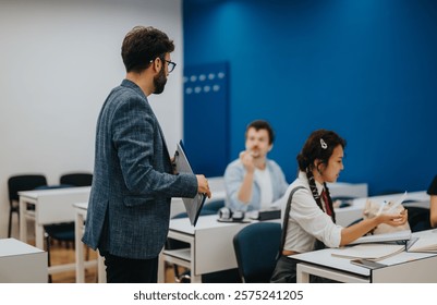A teacher interacts with attentive students during a classroom session. The modern classroom has a vibrant blue wall and is equipped with desks and chairs for learning.