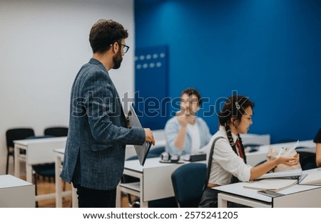 A teacher interacts with attentive students during a classroom session. The modern classroom has a vibrant blue wall and is equipped with desks and chairs for learning.