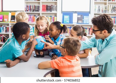 Teacher and kids discussing globe in library at school