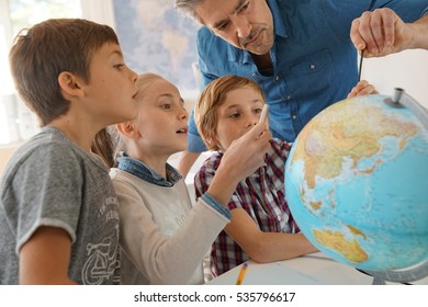 Teacher with kids in geography class looking at globe - Powered by Shutterstock