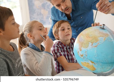 Teacher with kids in geography class looking at globe - Powered by Shutterstock