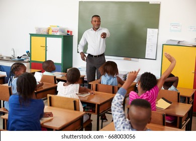 Teacher and kids with hands up in an elementary school class