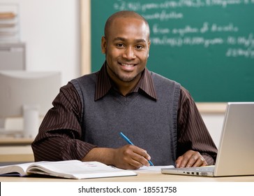 Teacher with laptop grading papers in school classroom