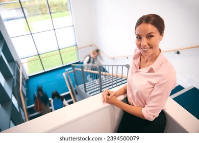 Teacher Looking Down On Group Of Secondary Or High School Pupils Inside School Building On Stairs