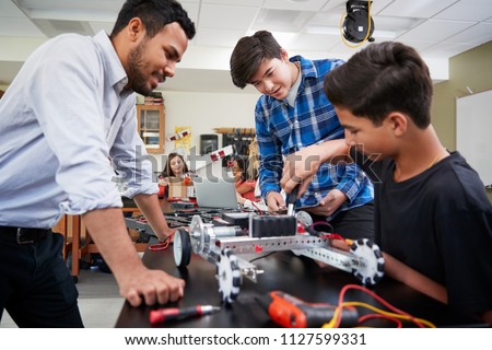 Teacher With Male Pupils Building Robotic Vehicle In Science Lesson