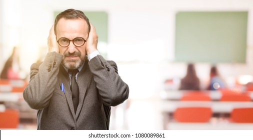 Teacher Man Using Glasses Covering Ears Ignoring Annoying Loud Noise, Plugs Ears To Avoid Hearing Sound. Noisy Music Is A Problem. At Classroom