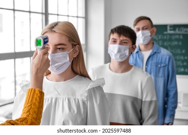 Teacher measuring student's temperature in classroom before exam - Powered by Shutterstock