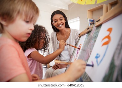 Teacher At Montessori School Helping Children In Art Class