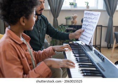 Teacher of music showing little schoolboy paper with notes while both sitting by piano keyboard at lesson - Powered by Shutterstock