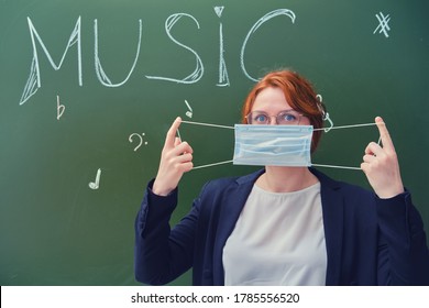 Teacher Music Shows How To Wear A Medical Mask On The Face. Female Teacher Next To The School Blackboard With The Words 