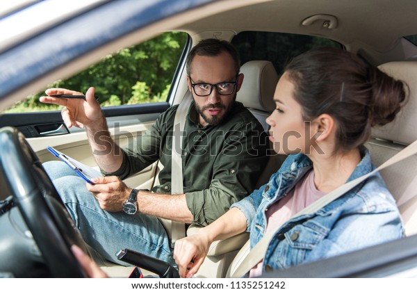 teacher pointing on something to student in car during\
driving test 