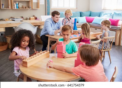 Teacher And Pupils Working At Tables In Montessori School