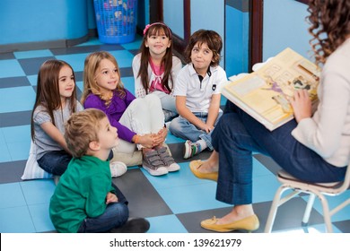 Teacher Reading Story Book To Children In Kindergarten