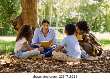 Teacher reading, tree or children with book for learning development, storytelling or growth in park. Smile, youth or happy educator with stories for education at a kids kindergarten school in nature