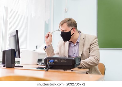 A Teacher At School At His Desk In A Protective Black Mask Is Trying To See Through His Glasses The Recording On The Computer.