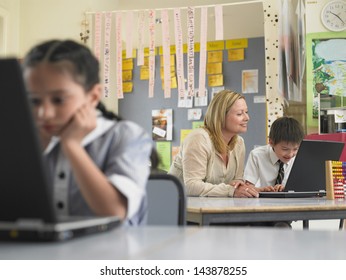 Teacher and schoolboy using laptop with girl in foreground at classroom