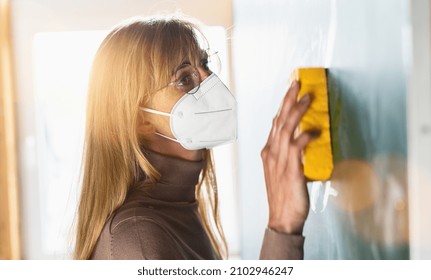 teacher at schoool cleaning blackboard or chalkboard with sponge at class room and wearing protective ffp2 KN95 face mask due to coronavirus pandemic