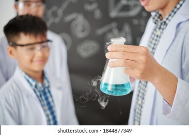 Teacher showing flask with smoking blue liquid to school students when explaining chemical reaction at science class - Powered by Shutterstock