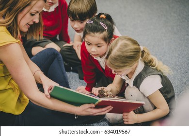 Teacher is sitting in the classroom with her primary school students, reading a story to them. - Shutterstock ID 634019567