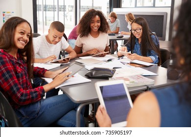Teacher sitting with high school students using tablets