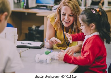 Teacher is sitting at the table in her classroom with her primary school students. They have built a car from recycled objects and crafts equipment and are testing that it works.  - Shutterstock ID 634019516