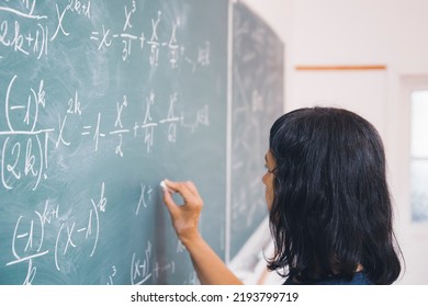 Teacher or student writing on blackboard during math lesson in school classroom.
