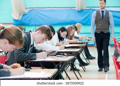 Teacher supervising middle school students taking examination at desks in school gymnastics hall - Shutterstock ID 1873350922