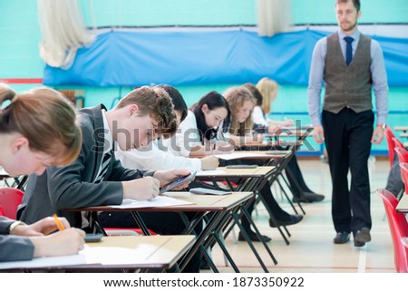 Teacher supervising middle school students taking examination at desks in school gymnastics hall