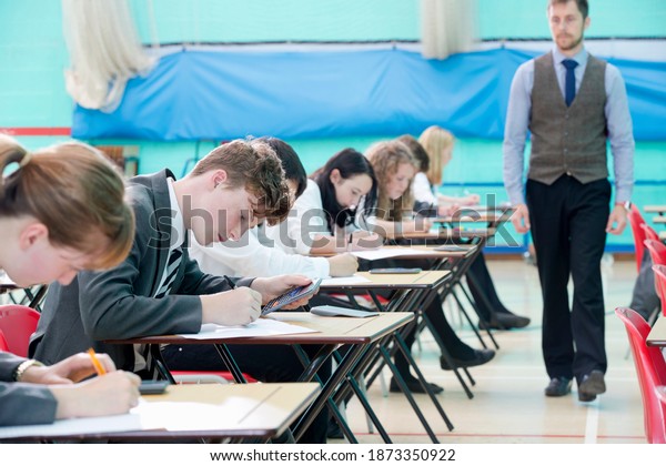 Teacher supervising middle school\
students taking examination at desks in school gymnastics\
hall