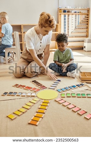 teacher talking to african american boy near colorful wooden bricks on floor in montessori school