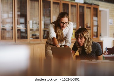 Teacher Talking To Female Student Sitting At The Desk Looking At Laptop. Teacher Helping A Student With Laptop During Her Lecture In University.