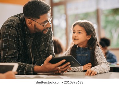 Teacher talking to his student while holding a digital tablet. Primary school educator giving a digital literacy lesson in an elementary school. Man mentoring young children in an education centre. - Powered by Shutterstock