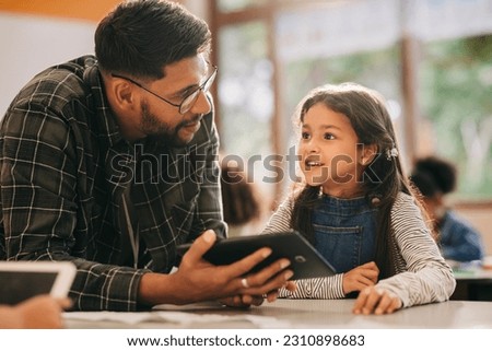 Teacher talking to his student while holding a digital tablet. Primary school educator giving a digital literacy lesson in an elementary school. Man mentoring young children in an education centre.