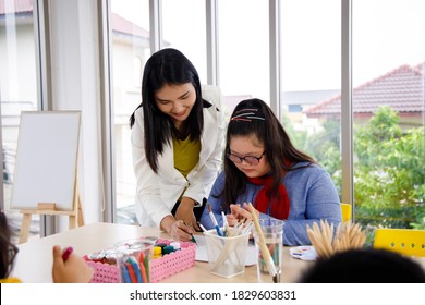Teacher teaches art to girl with Down's syndrome in classroom. Concept disabled kid learning.