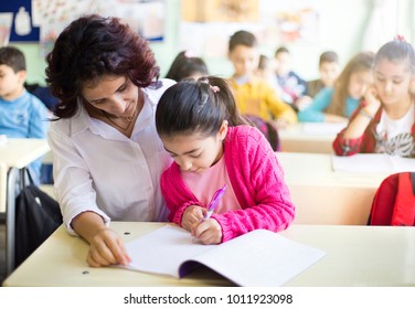 Teacher teaches to write to the girl student in the class